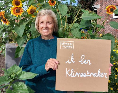 Gerd, Klimaatmaker in Olen, staat voor een zonnebloemenveld en houdt een kartonnen bordje vast met 'Ik ben Klimaatmaker'.