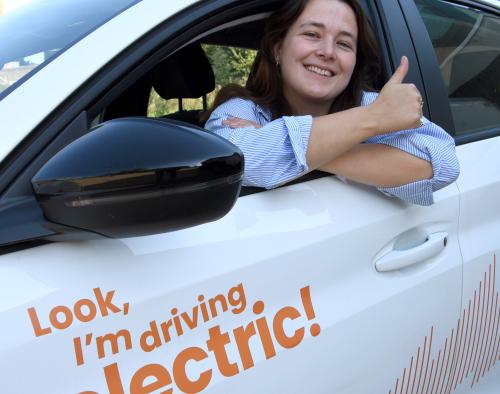 Vrouw zit in een elektrische deelauto en steekt haar duim omhoog.